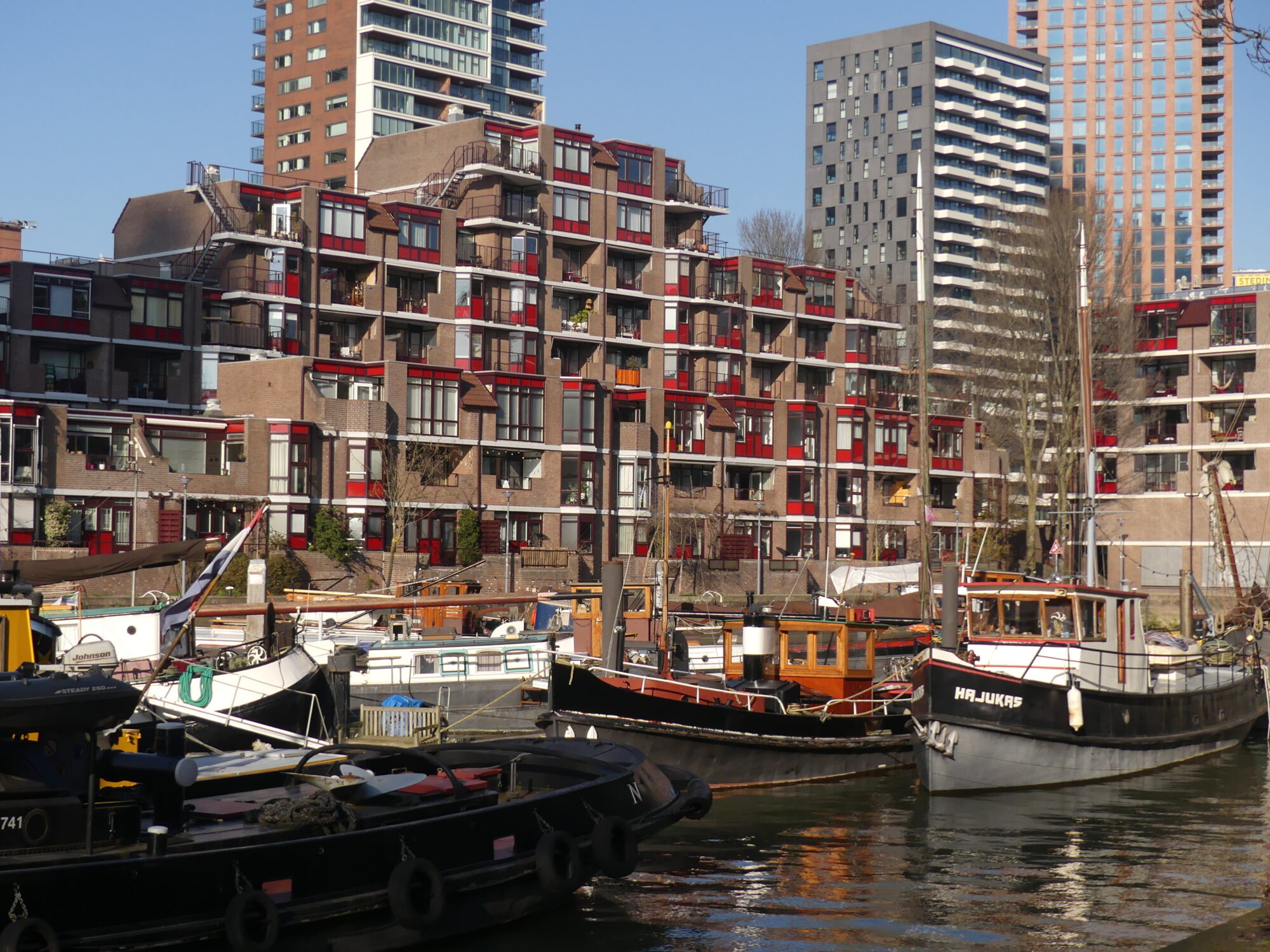 Small harbour with several boats lined with small buildings in the foreground and tower blocks in the background.