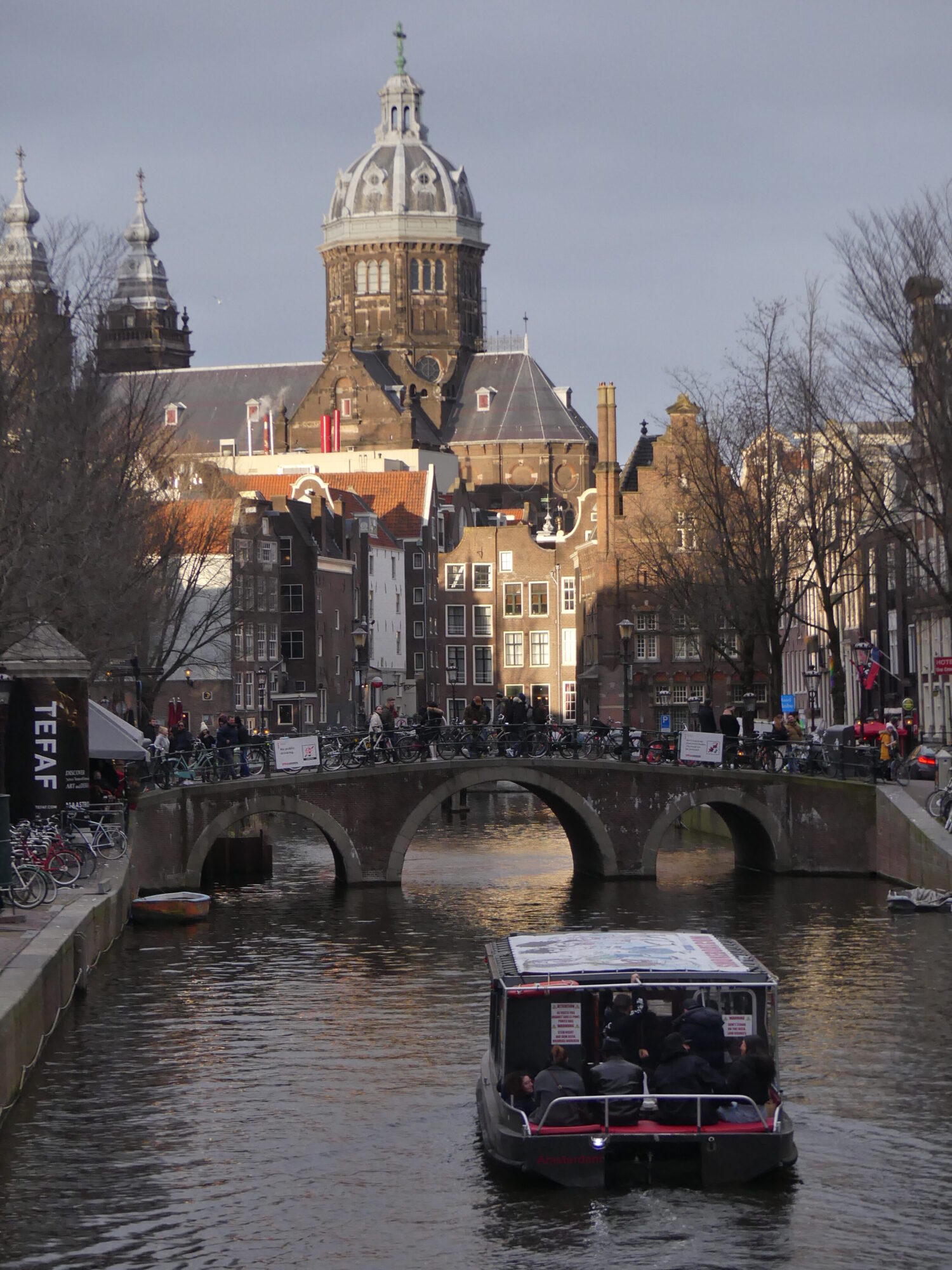 Petit bateau navigant sur le canal d'Amsterdam avec cathédrale en arrière plan.